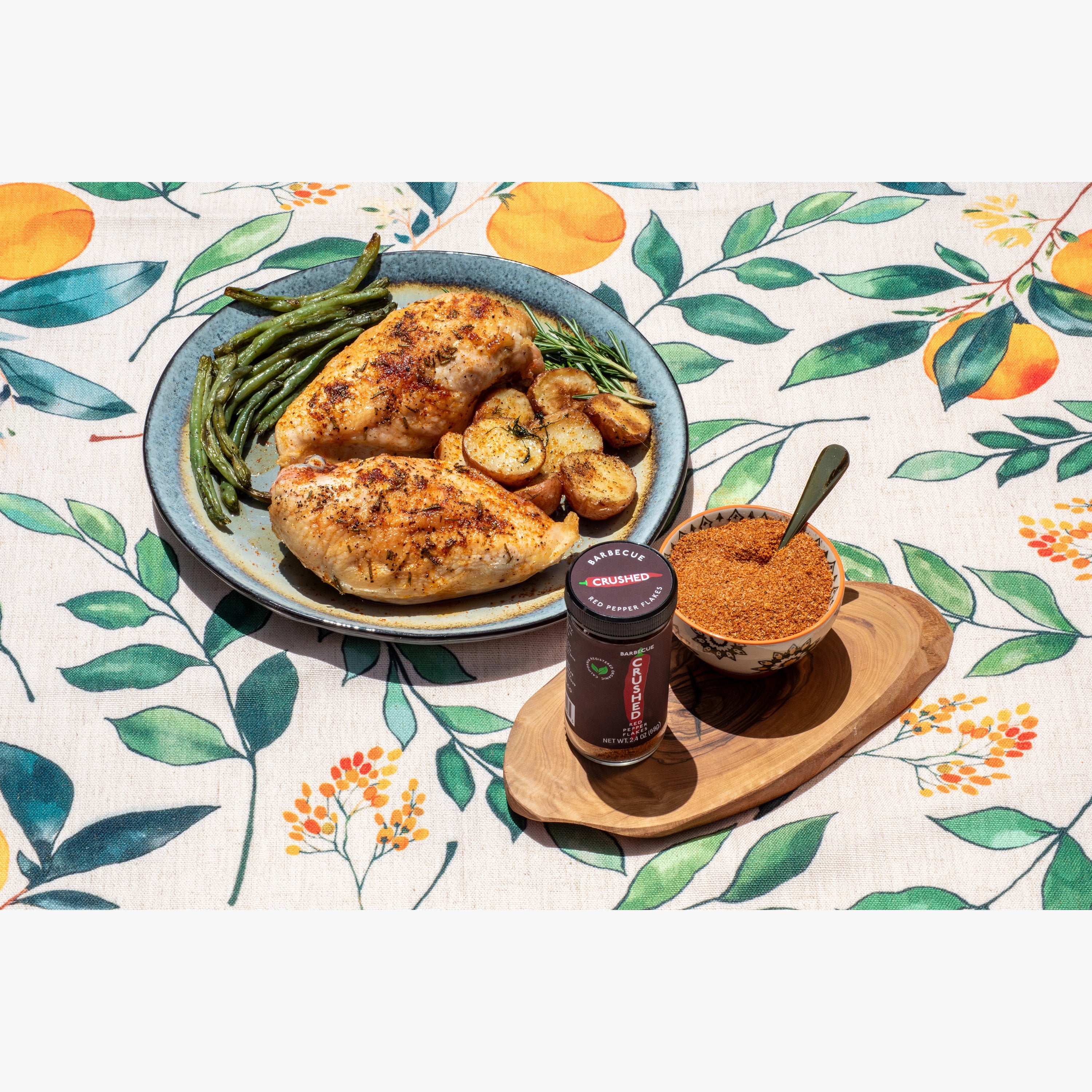 Plated dish of chicken with green beans and mushrooms on a floral tablecloth, accompanied by a jar of Barbecue Crushed Red Pepper.