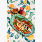 Original Crushed Red Pepper Flakes on a platter of roasted branzino with cherry tomatoes, lemon and rosemary on a decorative Italian table cloth