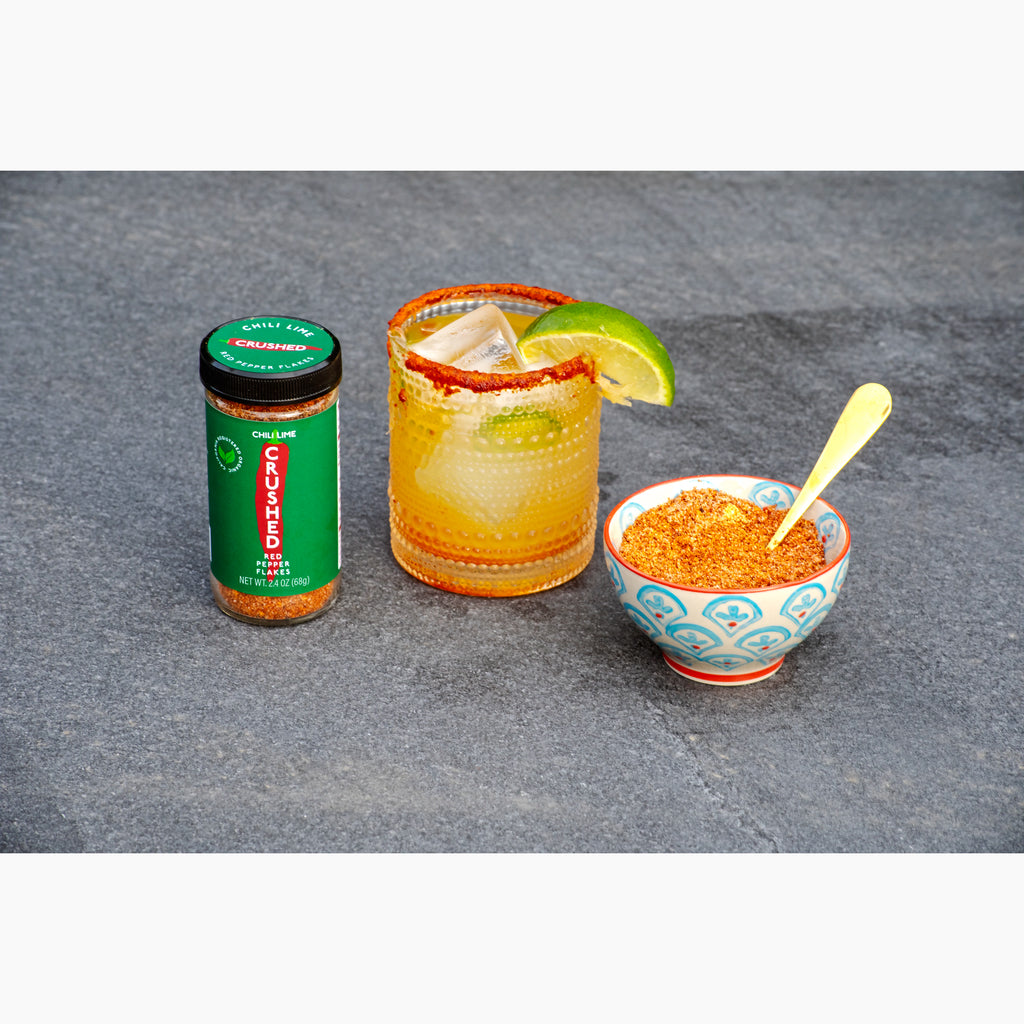 Jar of Chili Lime Crushed Red Pepper,  margarita cocktail with lime and chili lime spice rim, and bowl of Chili Lime Crushed Red Pepper on a gray slate surface.