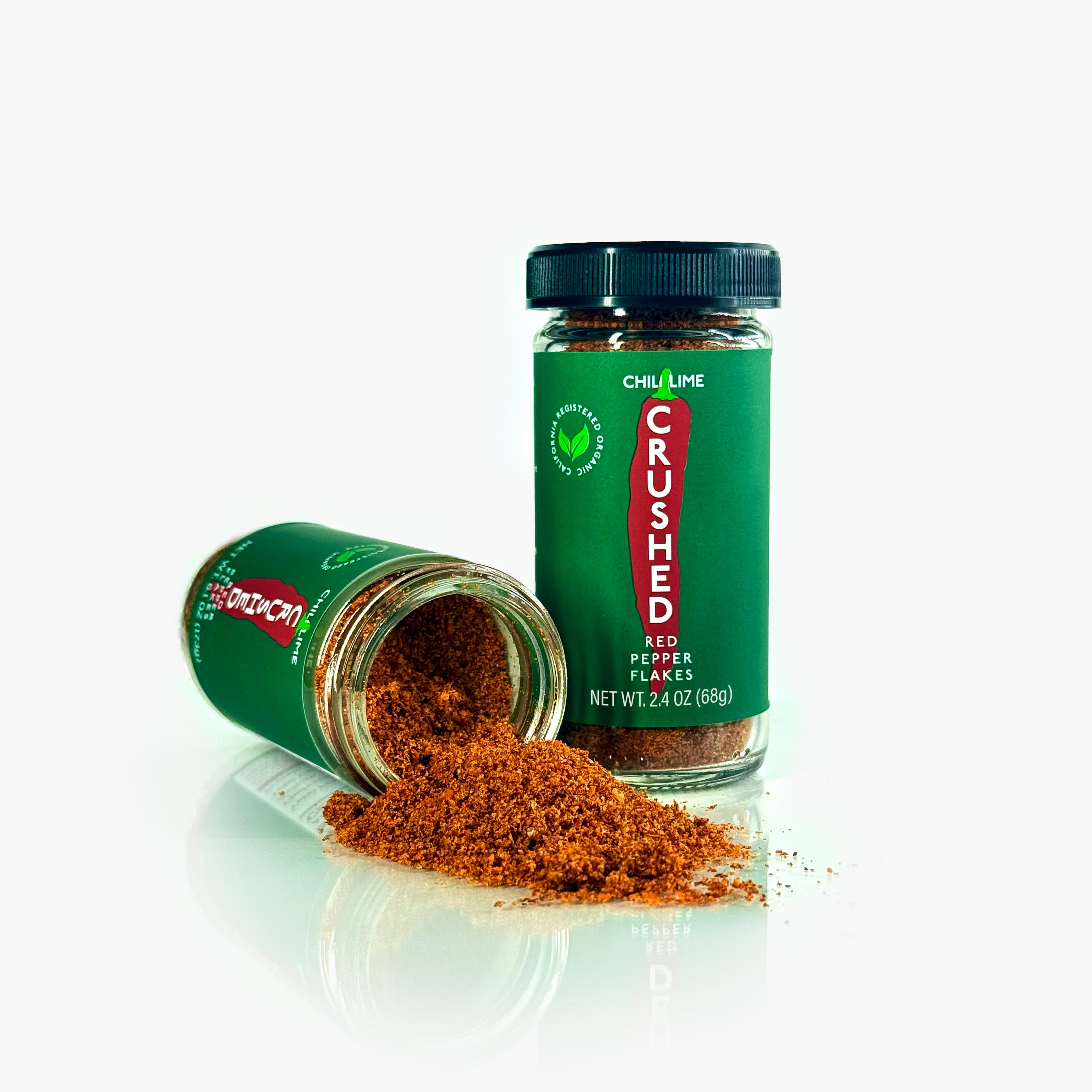 Two jars of Chili Lime Crushed Red Pepper Flakes on a white background, one on its side with the contents spilling out.